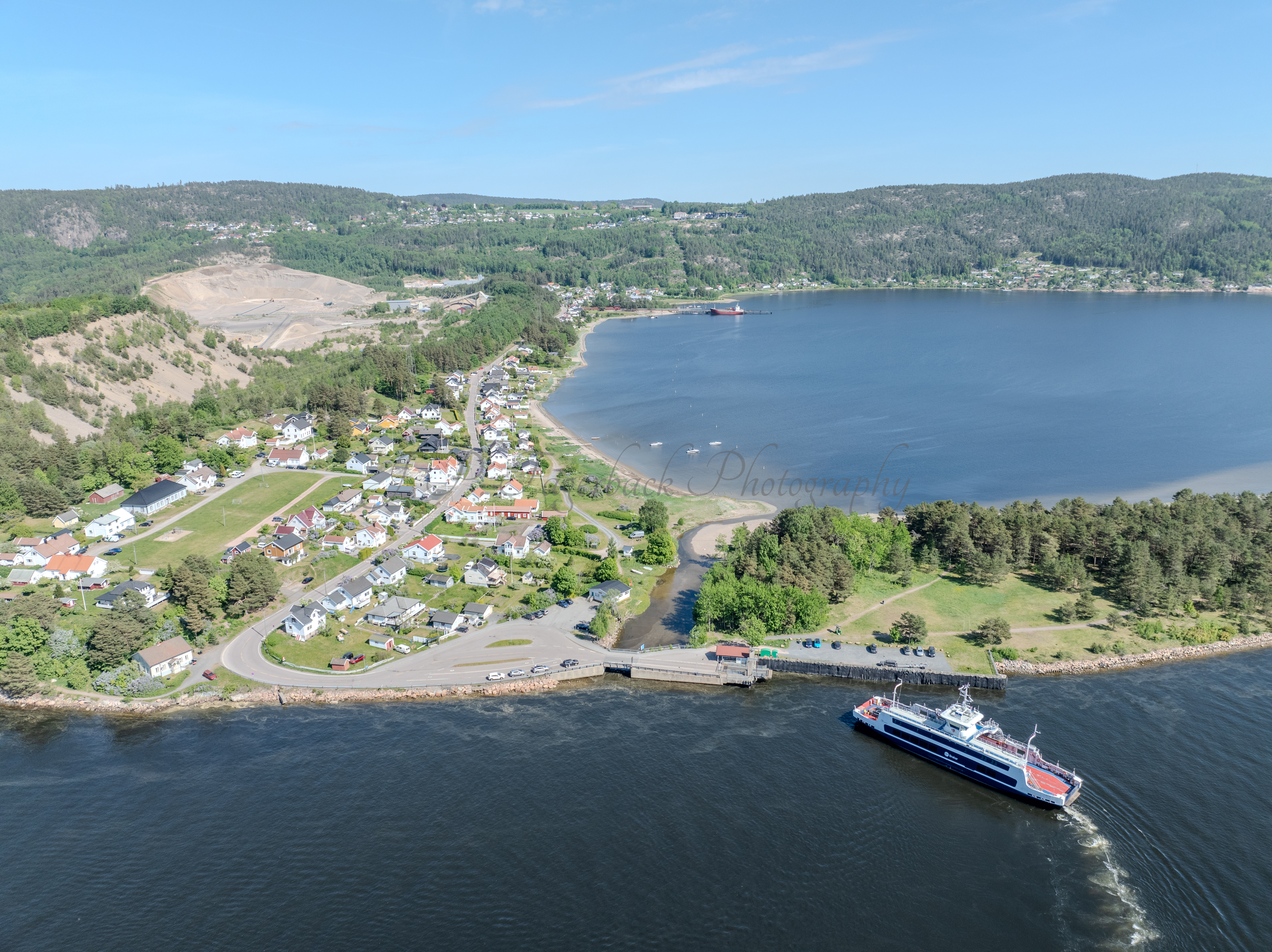 Buildings on both sides of a fjord where a ferry and other smaller boats are sailing