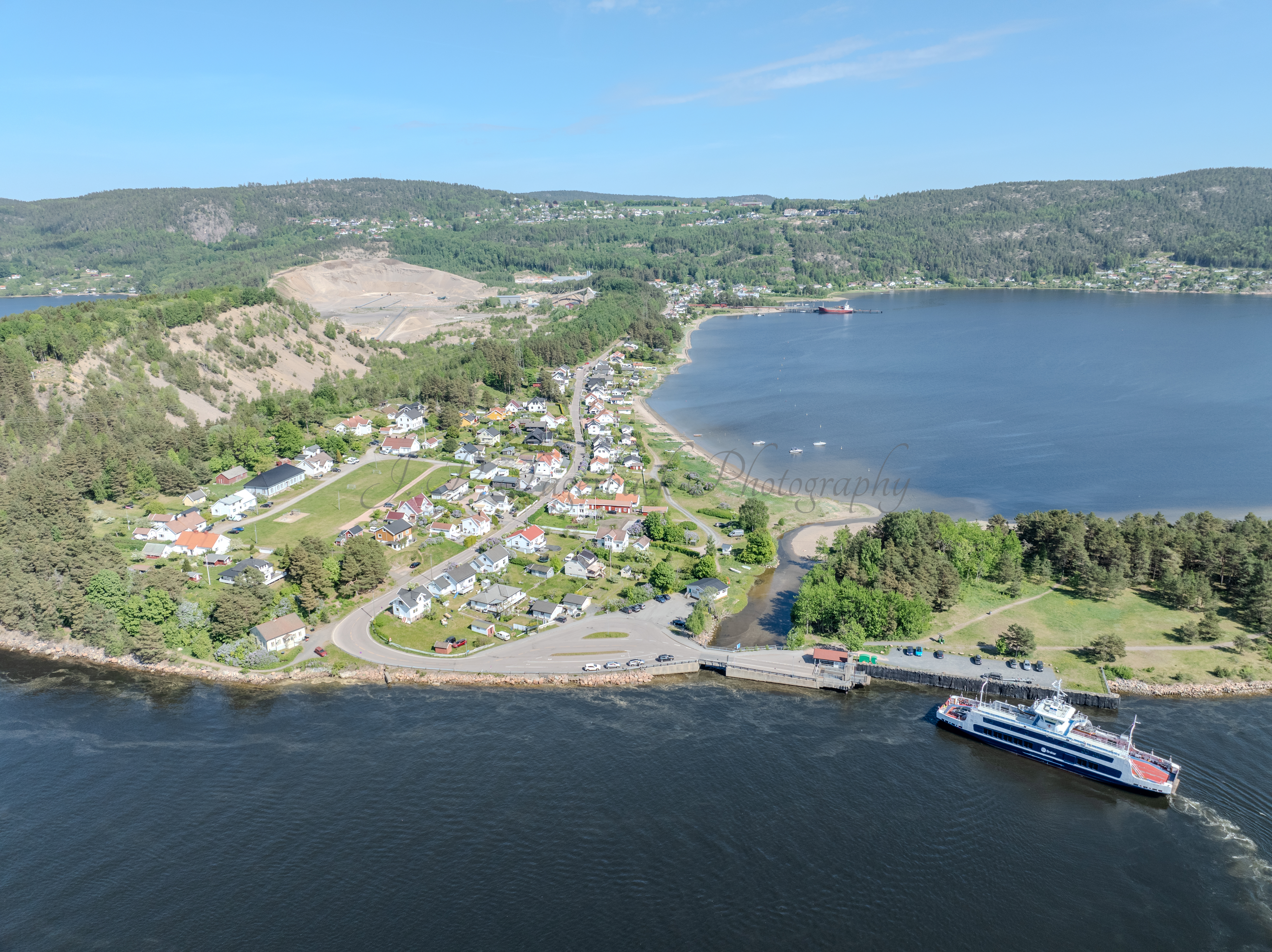Buildings on both sides of a fjord where a ferry and other smaller boats are sailing
