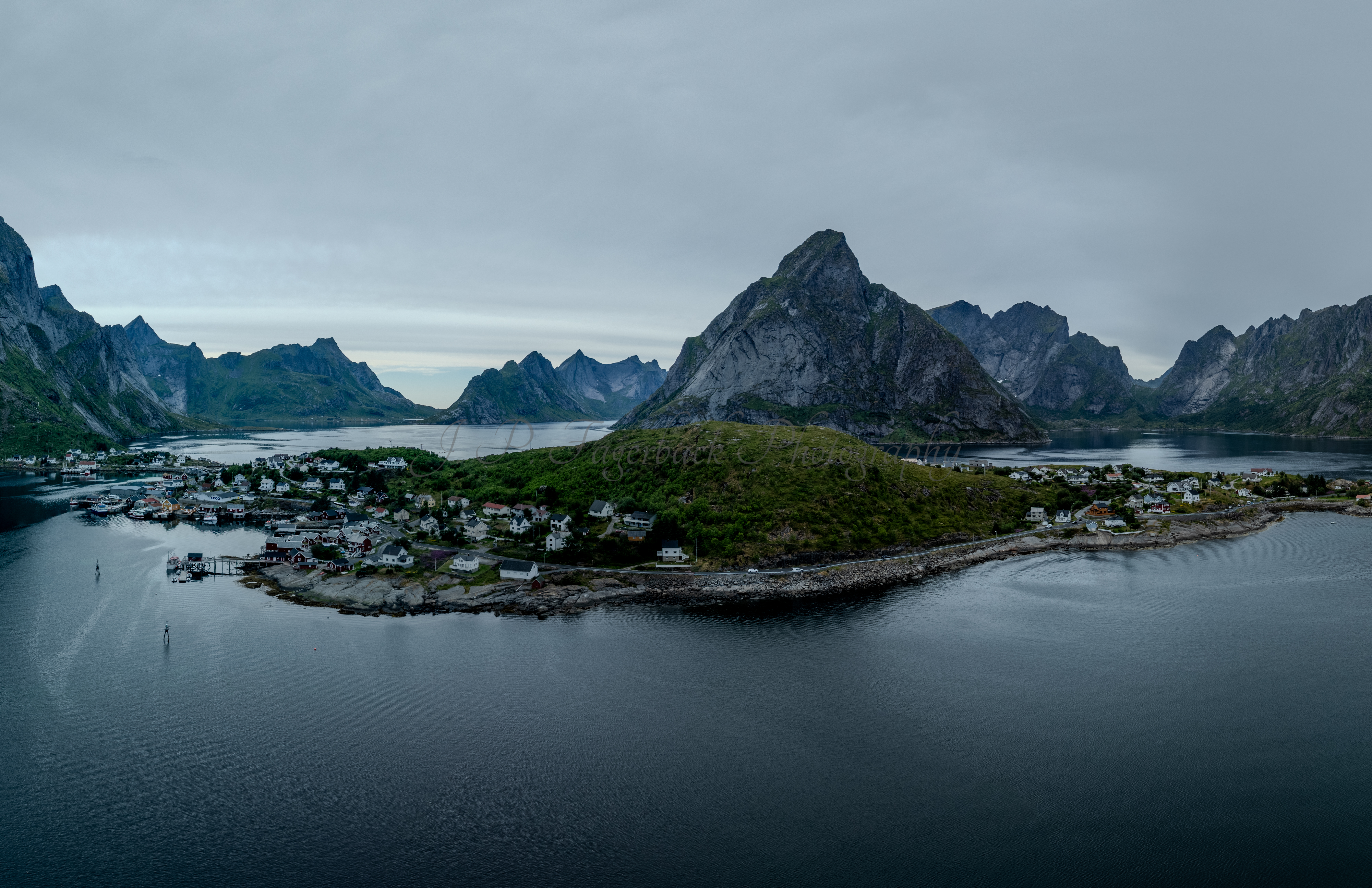 Buildings along the shore of a body of water with a mountain in the background on a gray day