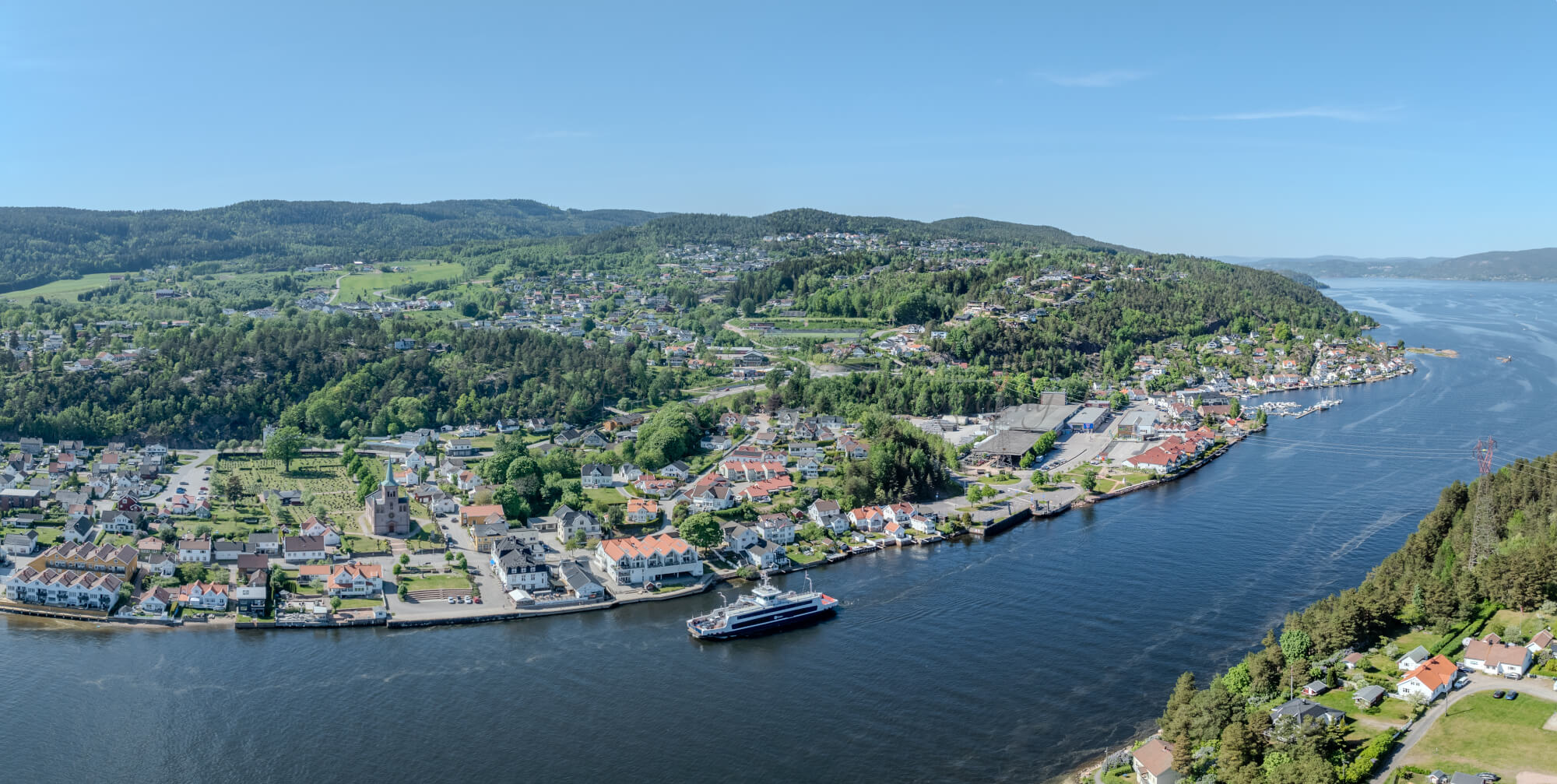 Buildings on both sides of a fjord where a ferry and other smaller boats are sailing