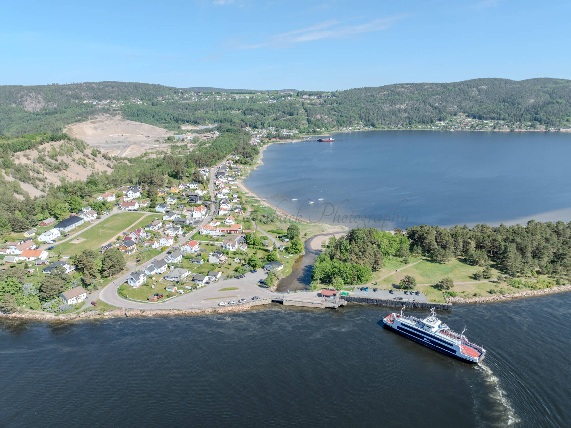Buildings on both sides of a fjord where a ferry and other smaller boats are sailing